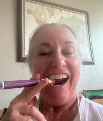Woman holding a purple and orange sleep spray near her mouth with a framed picture on the wall behind her.