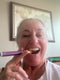 Woman holding a purple and orange sleep spray near her mouth with a framed picture on the wall behind her.