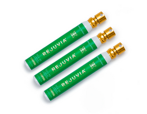 Three green REJUVIA products with gold caps on a white background